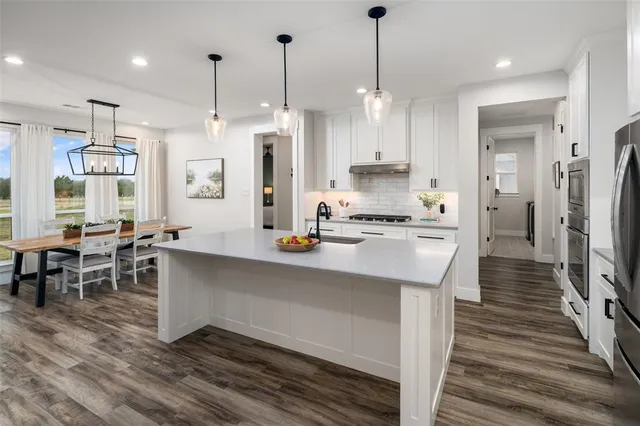 a large kitchen with stainless steel appliances kitchen island granite countertop a refrigerator a stove a sink and a dining table with wooden floor