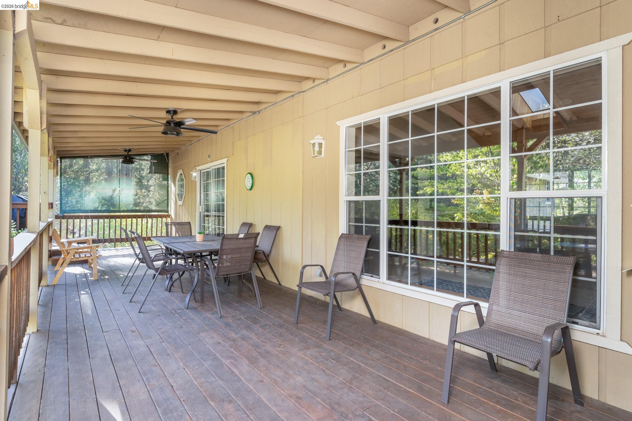 Expansive covered deck featuring wood plank flooring, a slatted wood ceiling, and multiple ceiling fans