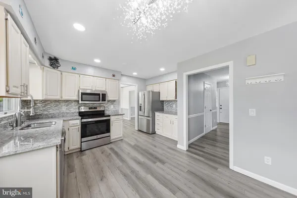 a kitchen with stainless steel appliances granite countertop a refrigerator oven a sink dishwasher and white cabinets with wooden floor