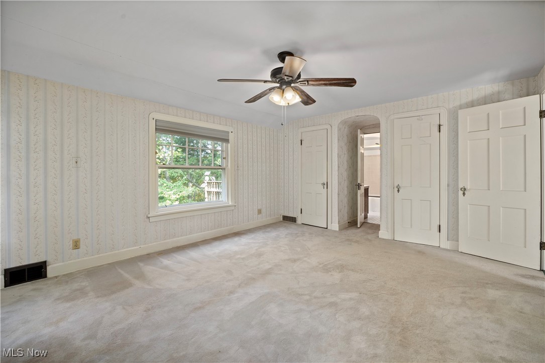 976 Gulf Road Elyria, OH 44035 - Photo 28 of 43 Unfurnished bedroom with wallpapered walls, arched walkways, carpet, a ceiling fan, and multiple closets