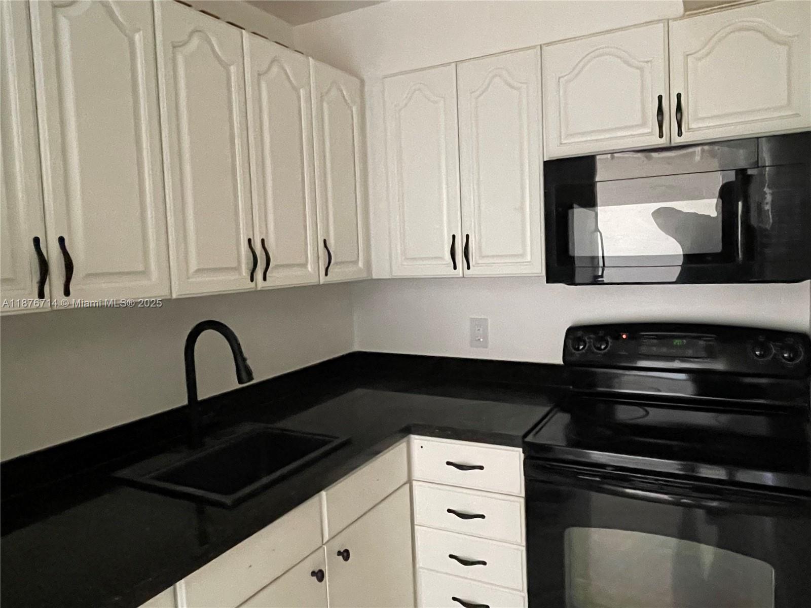 1881 Washington Avenue, Unit 15C Miami Beach, FL 33139 - Photo 19 of 30 a kitchen with granite countertop white cabinets and black appliances