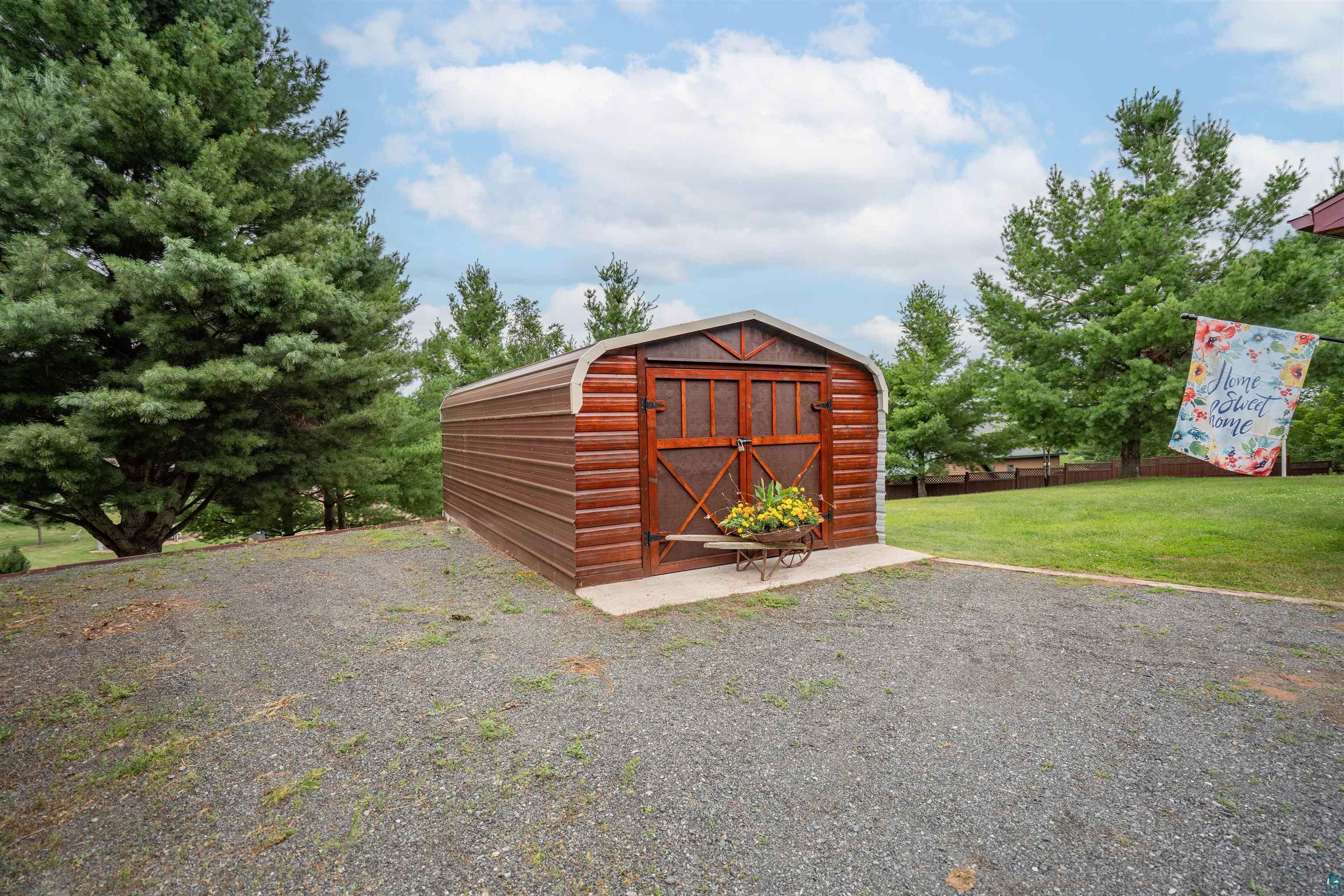 11911 East Rowe Road Lake Nebagamon, WI 54849 - Photo 25 of 61 Gravel driveway leading to a brown storage shed featuring a rounded roof and faux-wood paneled doors
