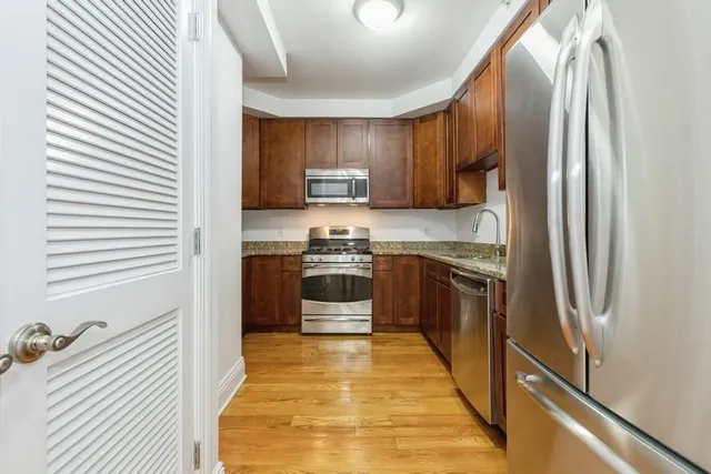 a kitchen with stainless steel appliances granite countertop a refrigerator a stove and a sink with wooden floor