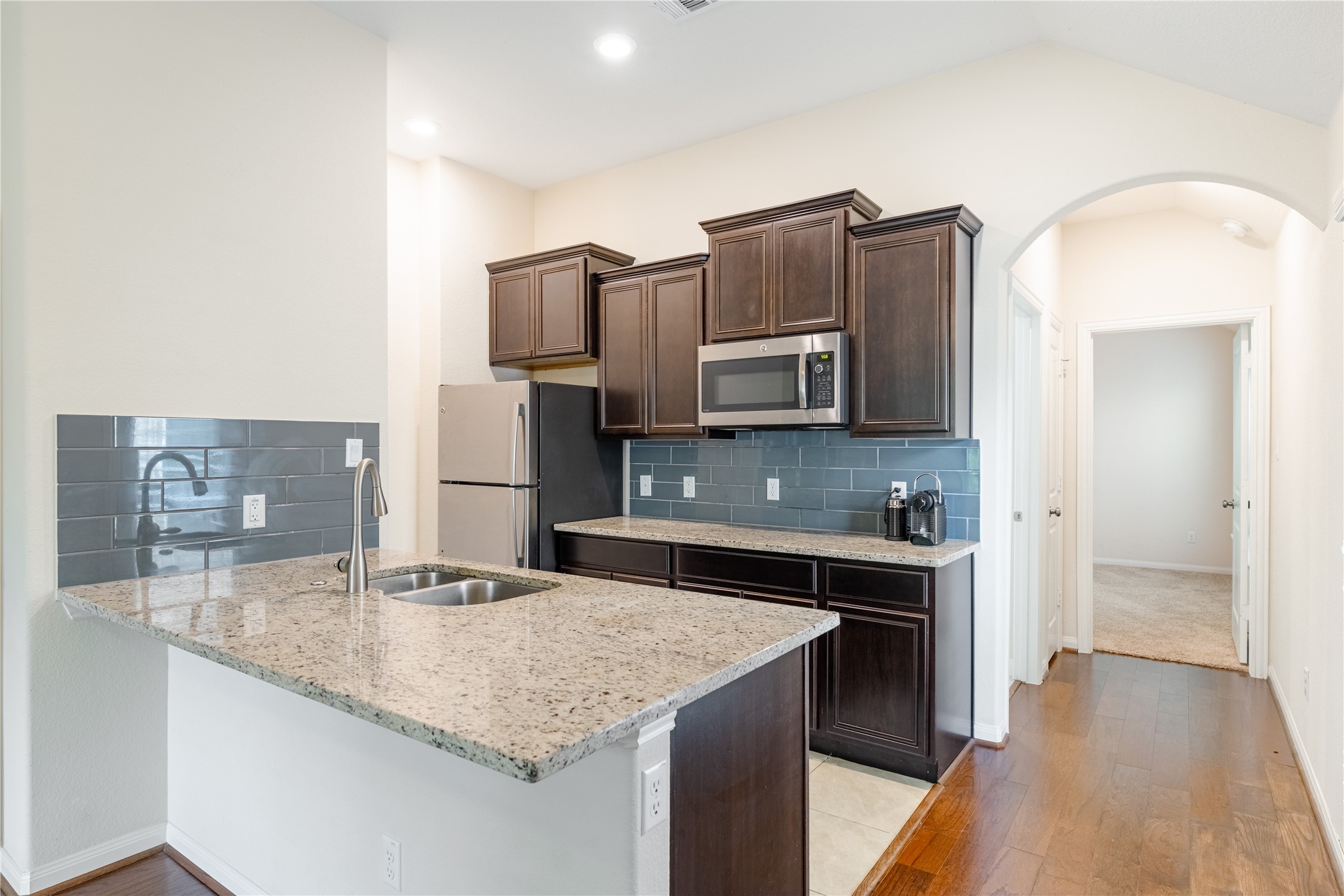 5012 Yucca Bloom Drive Georgetown, TX 78626 - Photo 16 of 35 Multi-Gen Kitchen featuring a peninsula with a double basin sink and a high-arc faucet, granite countertops, dark wood cabinetry, and a subway tile backsplash