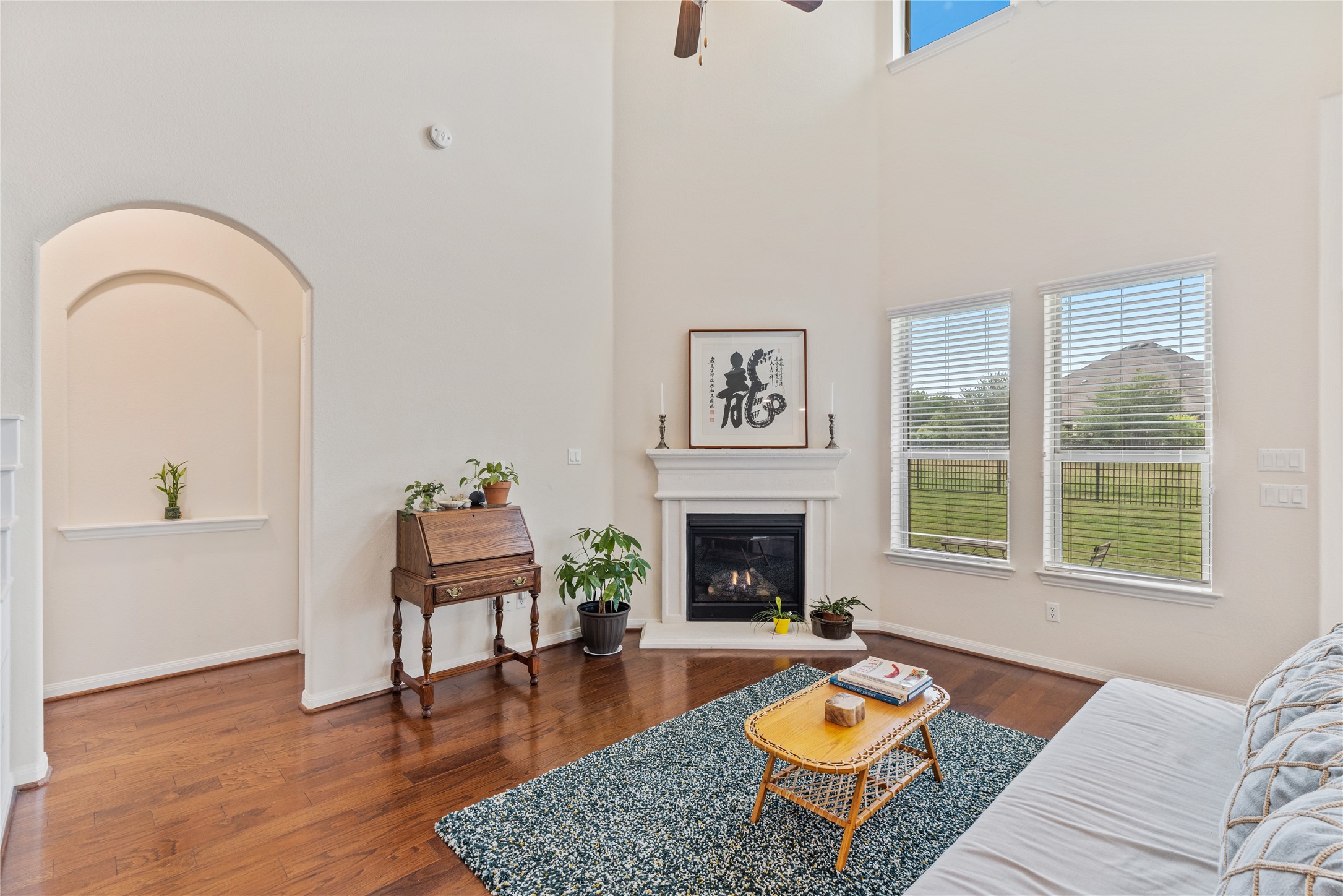 5012 Yucca Bloom Drive Georgetown, TX 78626 - Photo 2 of 35 Living area featuring a fireplace with a white mantel, large windows with blinds, wood-finish flooring, and a high ceiling