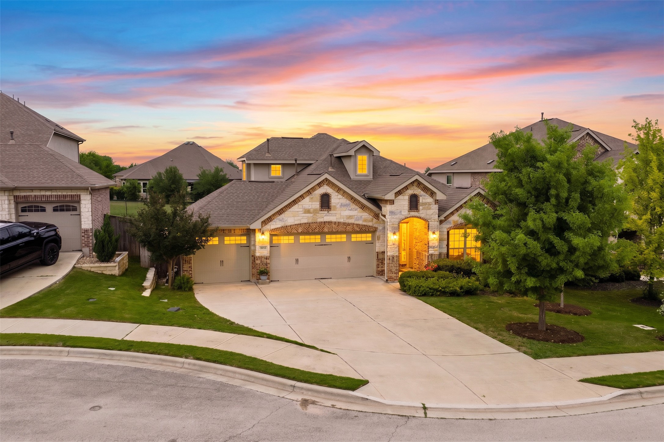 5012 Yucca Bloom Drive Georgetown, TX 78626 - Photo 29 of 35 Stone and brick façade residence featuring a multi-car driveway, two distinct garage doors, gabled rooflines, and mature landscaping