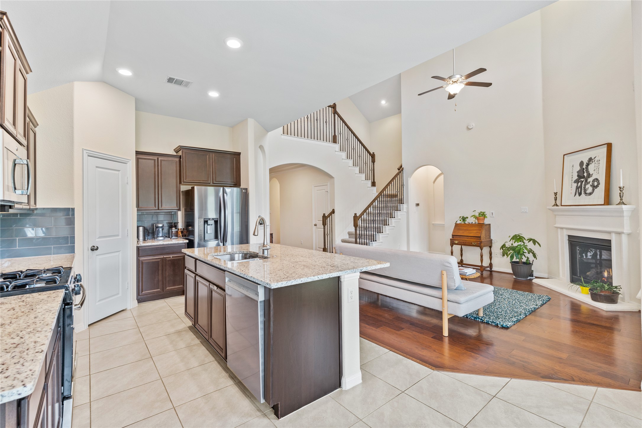 5012 Yucca Bloom Drive Georgetown, TX 78626 - Photo 9 of 35 Open-concept living space with a kitchen island featuring a stainless steel sink and appliances, granite countertops, tile flooring, and dark wood cabinetry
