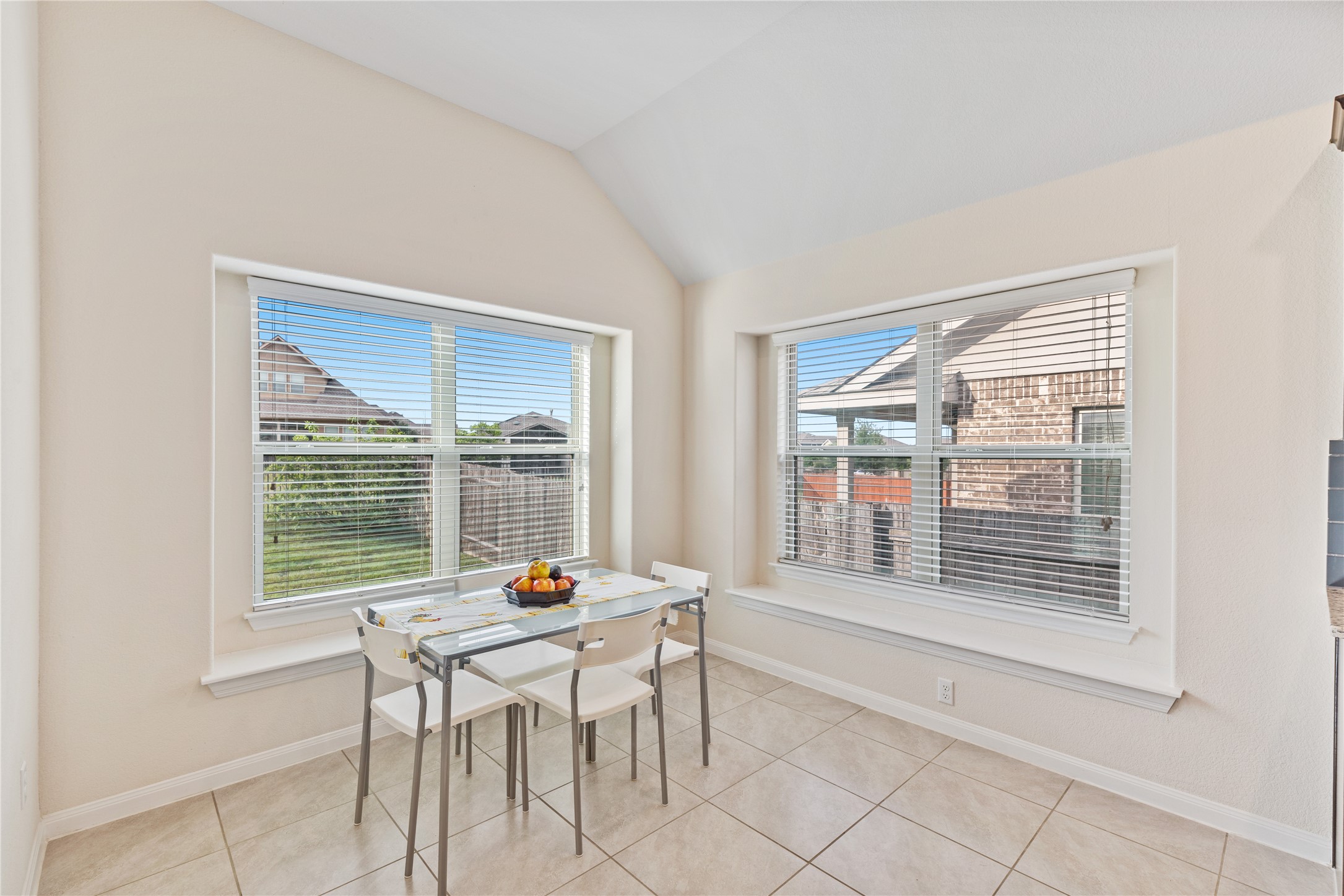 5012 Yucca Bloom Drive Georgetown, TX 78626 - Photo 10 of 35 Bright dining area featuring two large windows with blinds, a vaulted ceiling, and neutral tile flooring