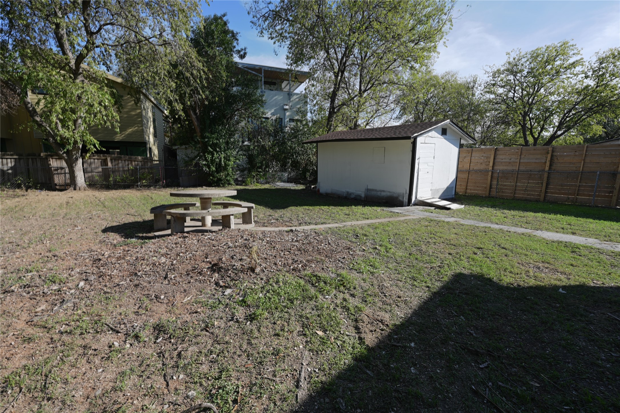 2311 South 3rd Street Austin, TX 78704 - Photo 14 of 14 Spacious backyard featuring a storage shed with a shingled roof, a wooden privacy fence, mature trees, and a concrete picnic table