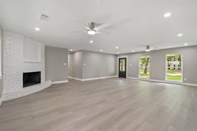 an empty room with wooden floor fireplace and windows