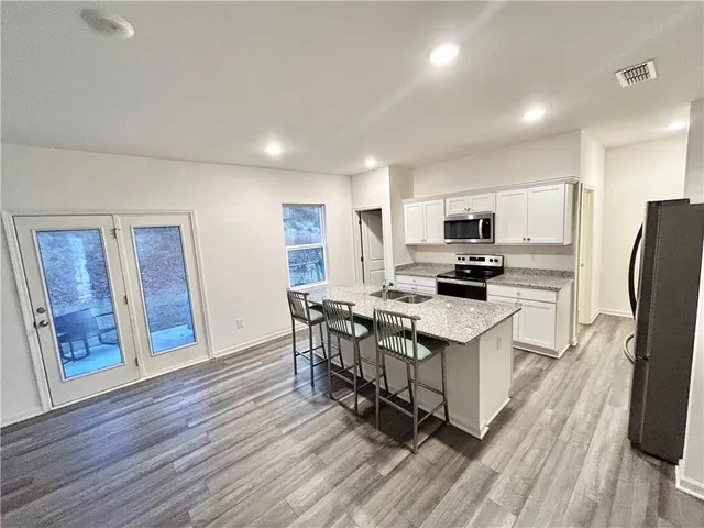 a kitchen with stainless steel appliances a microwave a stove a sink dishwasher a refrigerator and white cabinets with wooden floor