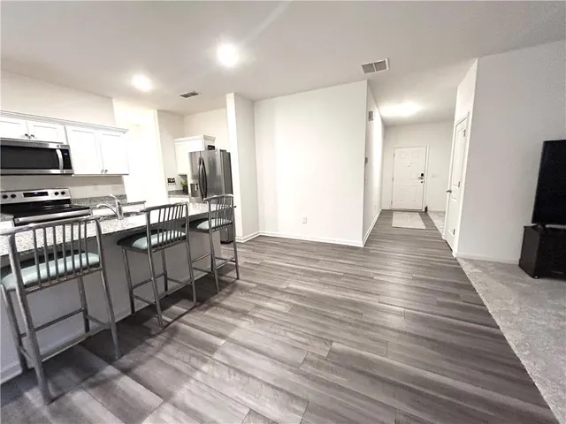 a kitchen with stainless steel appliances a stove top oven a sink dishwasher a refrigerator and white cabinets with wooden floor