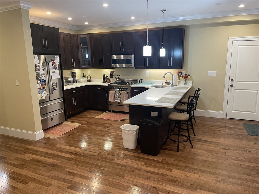 a kitchen with stainless steel appliances kitchen island granite countertop a refrigerator a stove a sink and a dining table with wooden floor