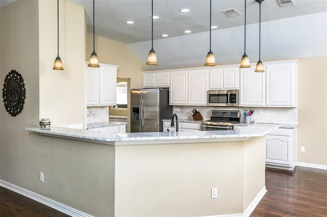 a kitchen with stainless steel appliances granite countertop a sink a stove a refrigerator and white cabinets with wooden floor