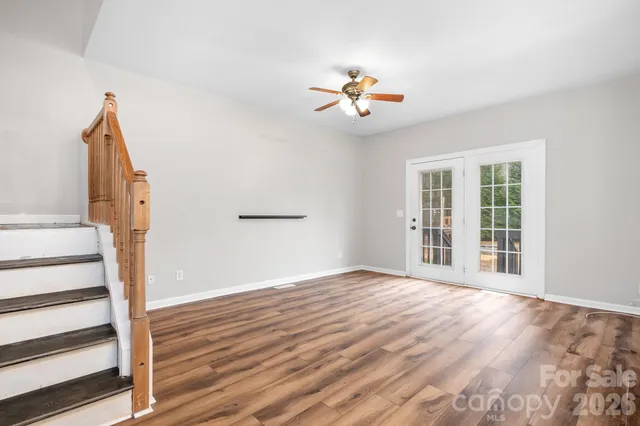 a view of an empty room with wooden floor and a chandelier fan