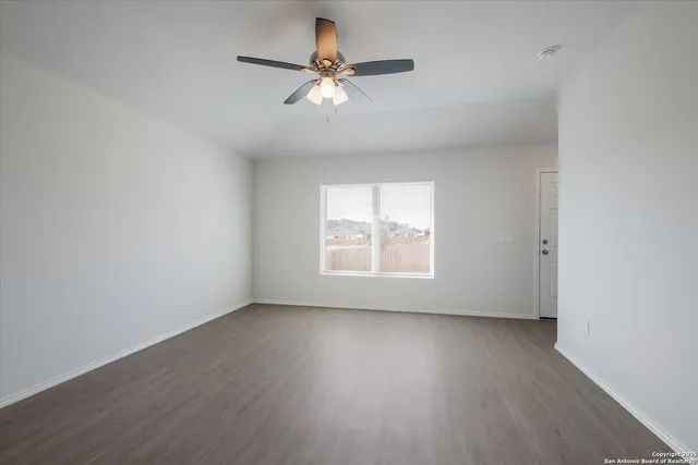 an empty room with wooden floor fan and windows