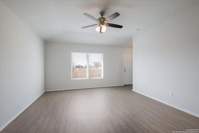 an empty room with wooden floor chandelier fan and windows