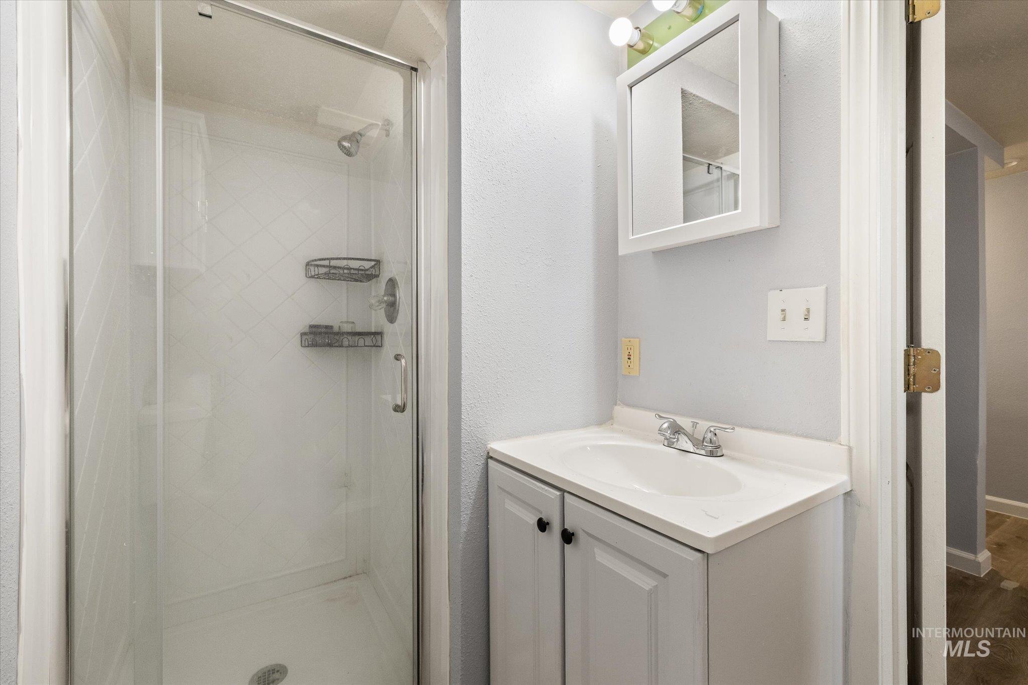 918 West 3rd Street Weiser, ID 83672 - Photo 29 of 36 Bathroom featuring a glass-enclosed shower with tiled walls, a white vanity with an integrated sink, and a wall-mounted medicine cabinet with an attached light fixture