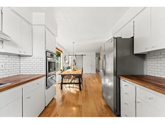 a kitchen with stainless steel appliances kitchen island granite countertop a refrigerator a sink dishwasher and white cabinets with wooden floor