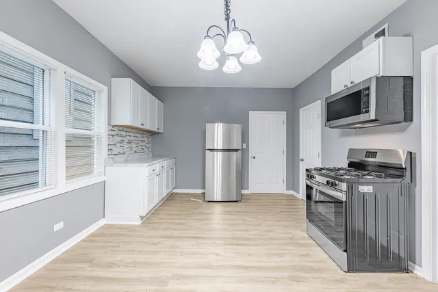 a kitchen with stainless steel appliances granite countertop a stove top oven a refrigerator cabinets and a wooden floor