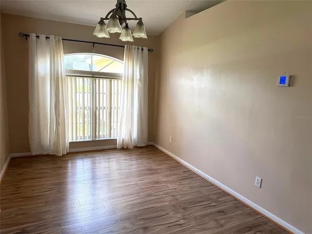 an empty room with wooden floor chandelier and windows
