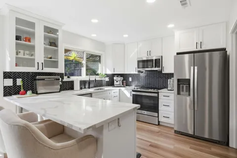 a kitchen with a sink dishwasher a stove and white cabinets with wooden floor