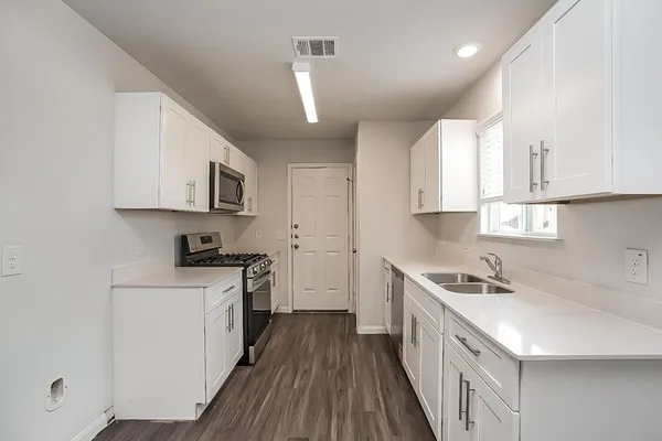 a kitchen with stainless steel appliances a sink dishwasher a stove top oven a refrigerator with white cabinets and wooden floor