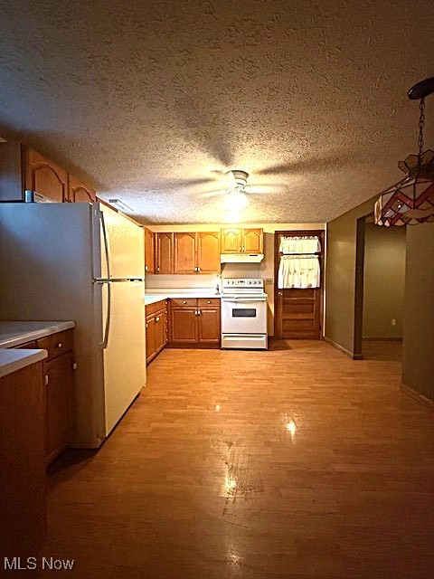 Kitchen with white appliances, a textured ceiling, brown cabinets, under cabinet range hood, and light wood-style flooring