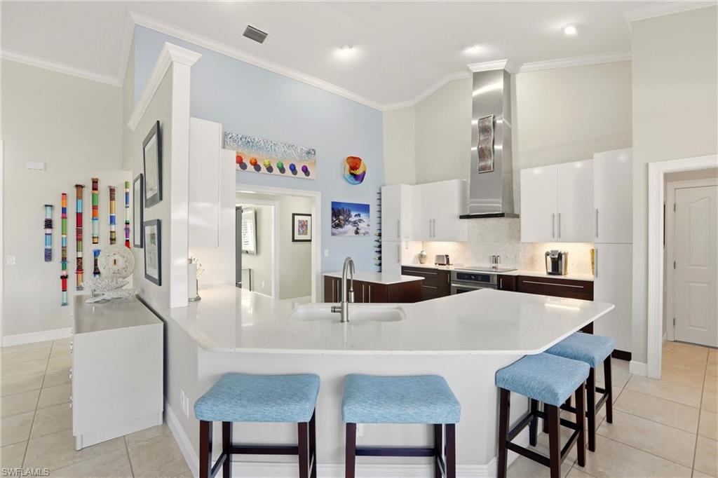 11180 Phoenix Way Naples, FL 34119 - Photo 11 of 43 Two tone kitchen with dual tone cabinets, light tile patterned flooring, a peninsula, a kitchen bar, and backsplash