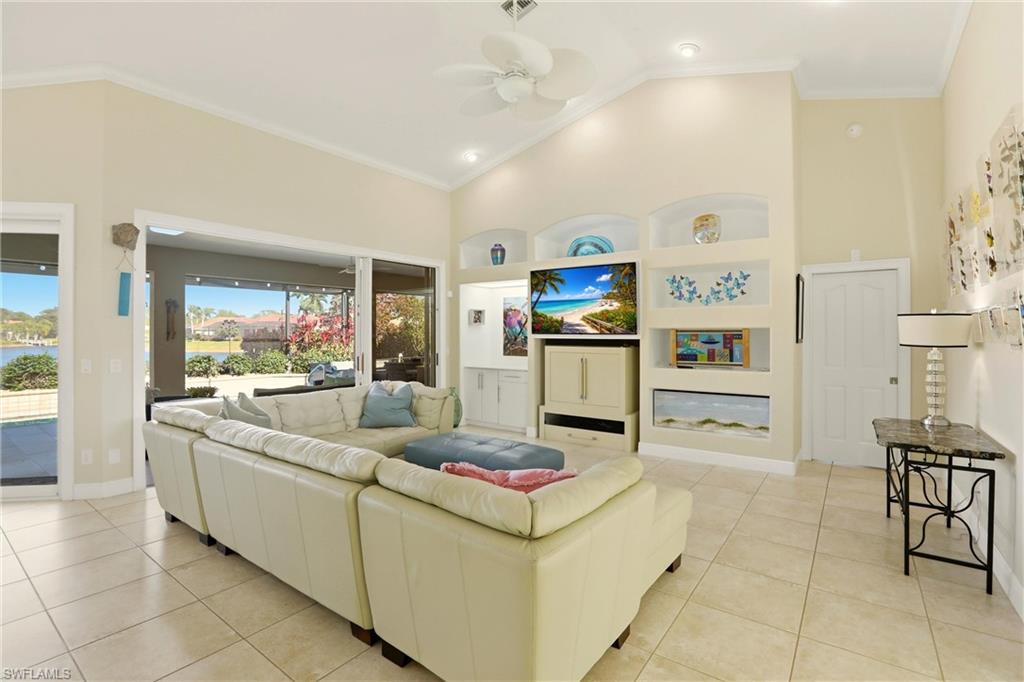 11180 Phoenix Way Naples, FL 34119 - Photo 4 of 43 Living room with built in shelves, a ceiling fan, crown molding, vaulted ceiling, and light tile patterned floors