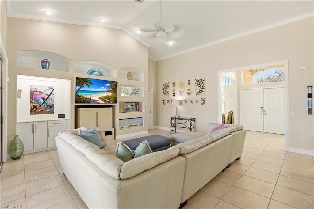 11180 Phoenix Way Naples, FL 34119 - Photo 5 of 43 Living room featuring built in features, a ceiling fan, vaulted ceiling, crown molding, and light tile patterned floors