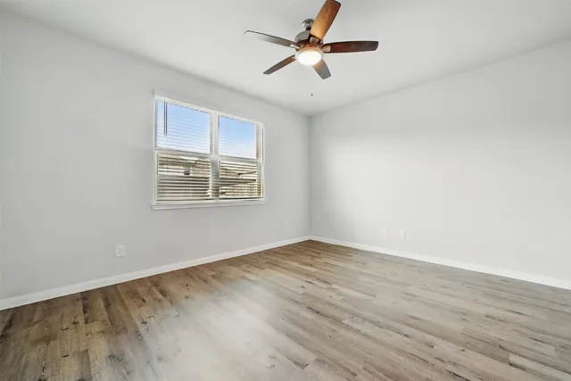 an empty room with wooden floor ceiling fan and windows