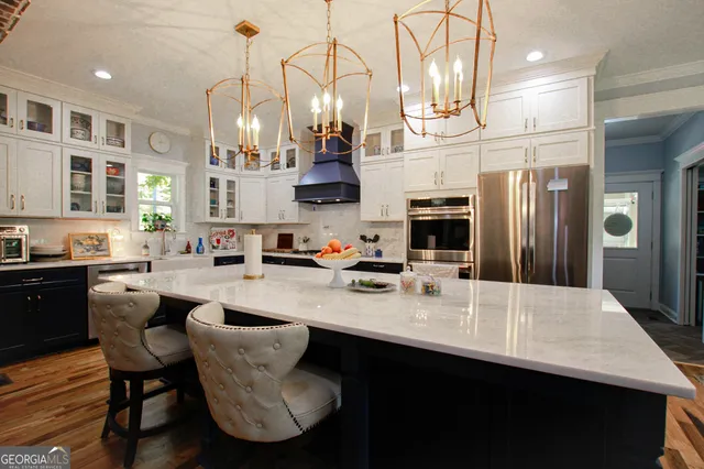 a kitchen with stainless steel appliances granite countertop a sink dishwasher a refrigerator a stove a kitchen island and chairs with wooden floor