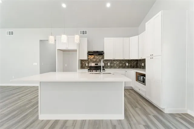 a kitchen with stainless steel appliances a microwave a stove a sink dishwasher and white cabinets with wooden floor