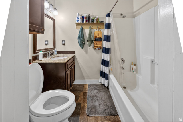 730 East 200 North Logan, UT 84321 - Photo 13 of 28 Bathroom featuring wood-finish flooring, a white toilet, a dark wood-finish vanity with a light-colored countertop, and a built-in shower/tub combination