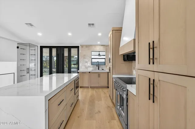 a kitchen with stainless steel appliances granite countertop a refrigerator a sink a stove and white cabinets with wooden floor