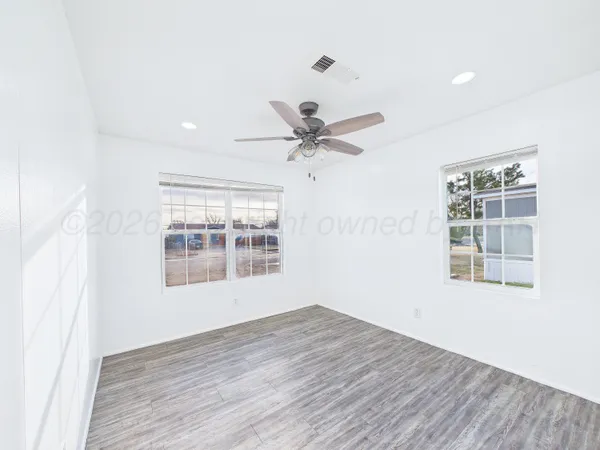 an empty room with wooden floor fan and windows