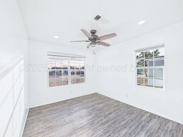 an empty room with wooden floor chandelier fan and windows