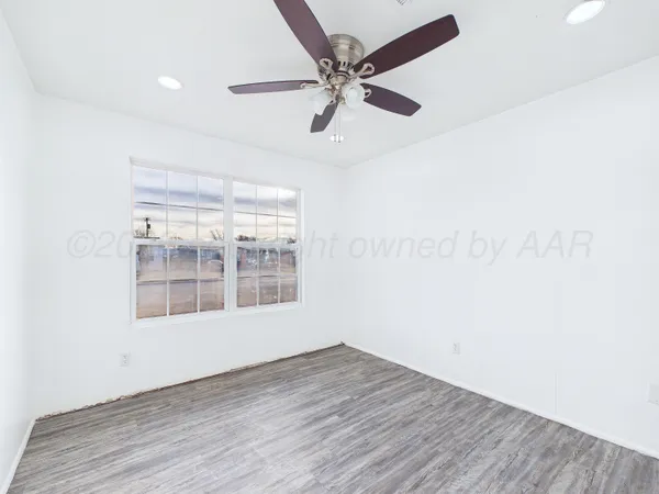 an empty room with wooden floor fan and windows