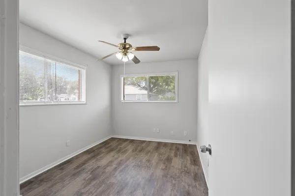 an empty room with wooden floor ceiling fan and window