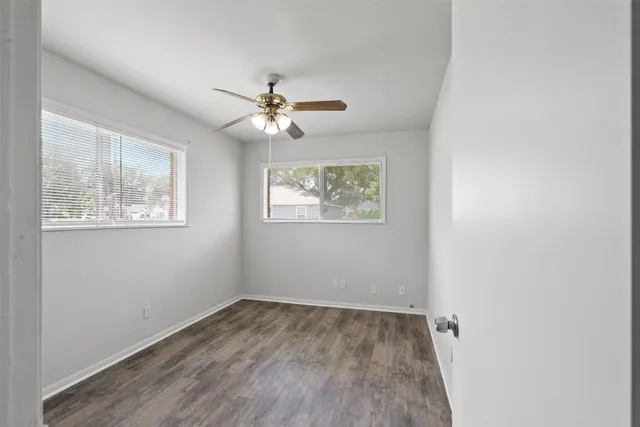 an empty room with wooden floor ceiling fan and window
