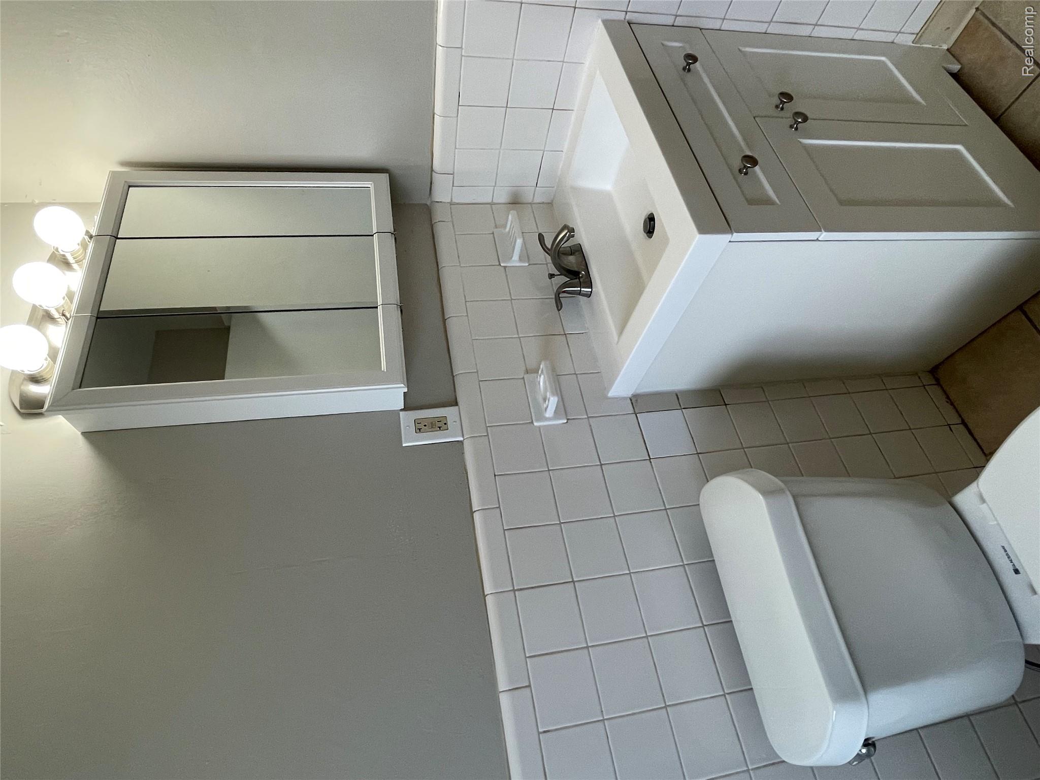 1173 Featherstone Road Pontiac, MI 48342 - Photo 16 of 23 White tiled walls with a vanity featuring a single basin sink and dual cabinet doors