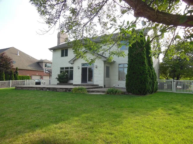 a view of a white house next to a yard with a large trees