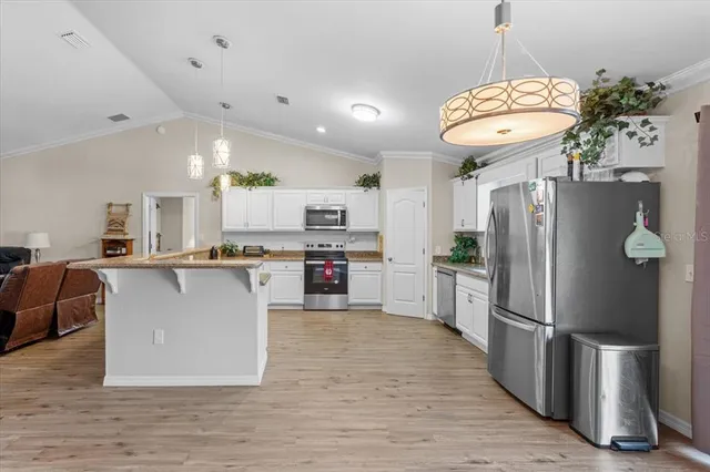 a large kitchen with stainless steel appliances granite countertop a refrigerator a stove a sink dishwasher a oven and a dining table with wooden floor