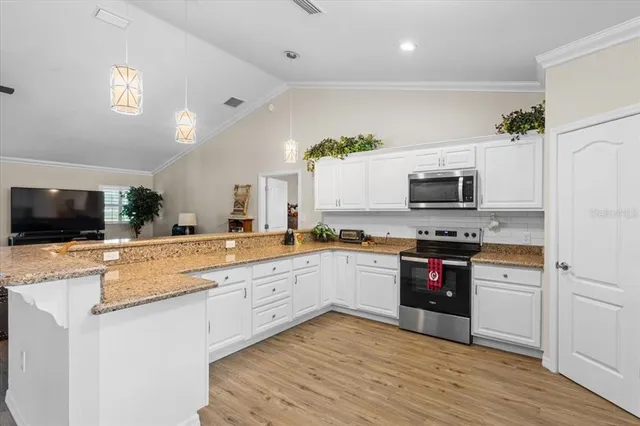 a large kitchen with granite countertop a stove top oven a sink dishwasher and white cabinets with wooden floor