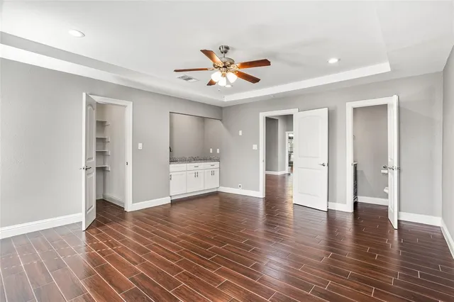 a view of an empty room with wooden floor and a ceiling fan