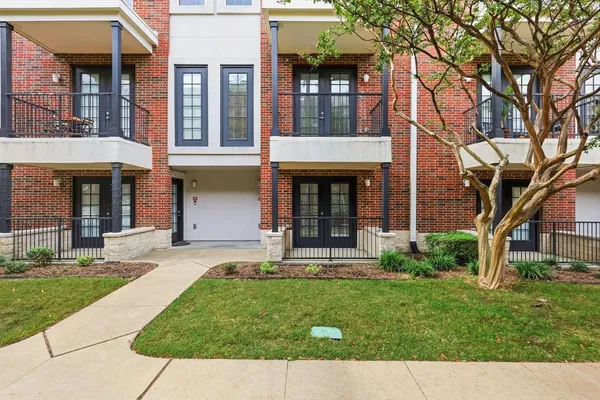 front view of a brick house with a yard and large trees