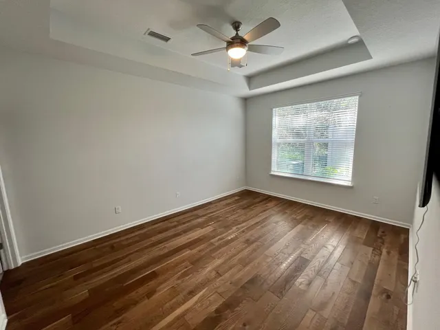 an empty room with wooden floor chandelier fan and windows
