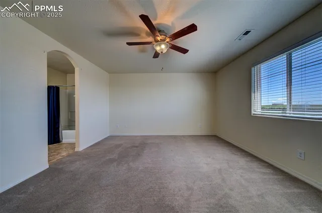 an empty room with ceiling fan and windows