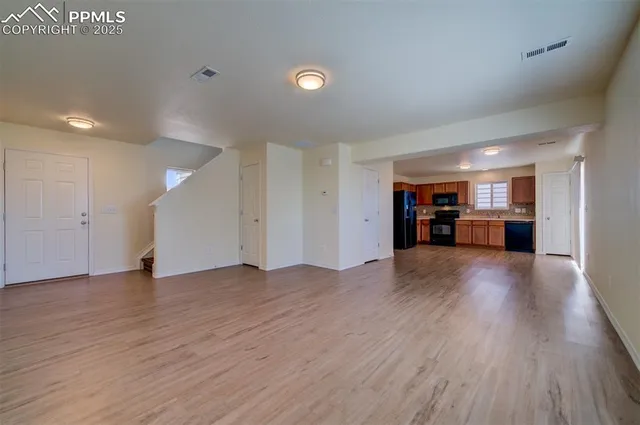 a view of an empty room with wooden floor and kitchen